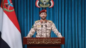A Houthi military spokesman at a podium in front of Yemeni flags