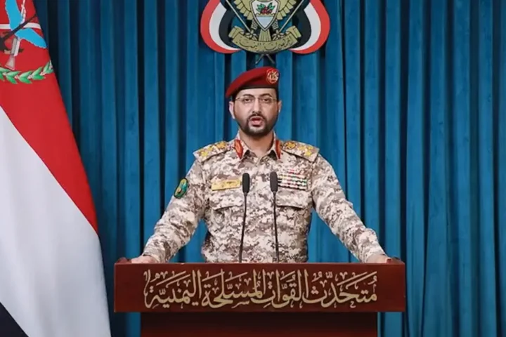 A Houthi military spokesman at a podium in front of Yemeni flags
