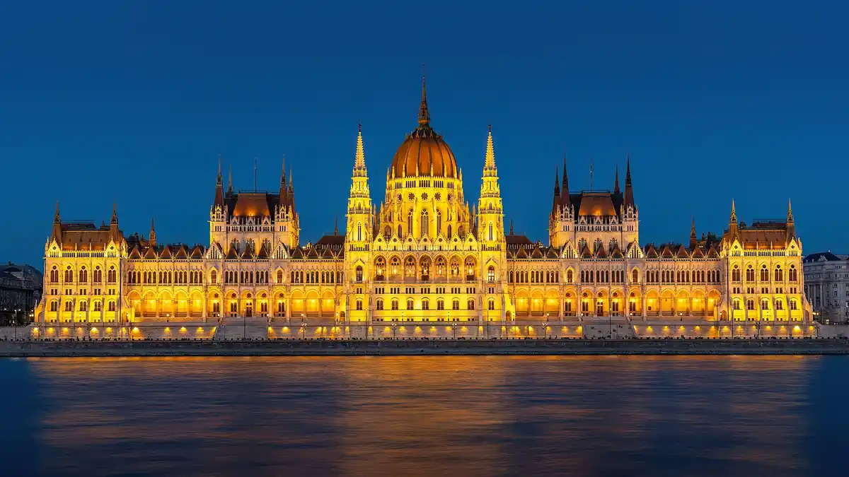 The Hungarian Parliament building in Budapest lit up at dusk beside the Danube