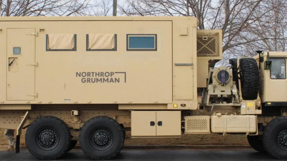 Tan shelter van with the Northrop Grumman logo mounted on a military truck, shown with its sides closed