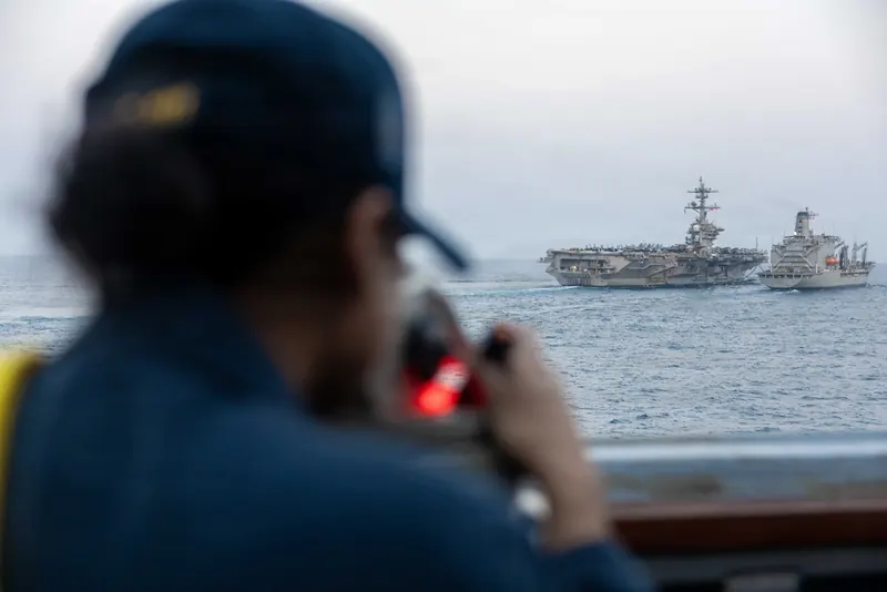 A U.S. sailor aboard the destroyer USS Spruance watches the aircraft carrier USS Abraham Lincoln take on supplies from the oiler USNS Henry J. Kaiser at sea during Operation Epic Fury