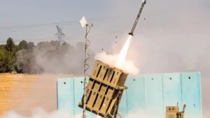 An Iron Dome launcher firing a Tamir interceptor, with smoke and a rocket plume against a hazy sky