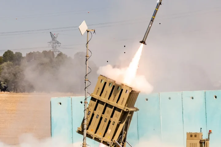 An Iron Dome launcher firing a Tamir interceptor, with smoke and a rocket plume against a hazy sky