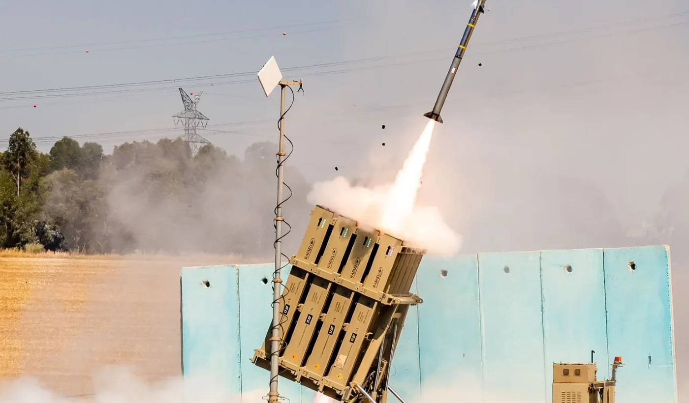 An Iron Dome launcher firing a Tamir interceptor, with smoke and a rocket plume against a hazy sky
