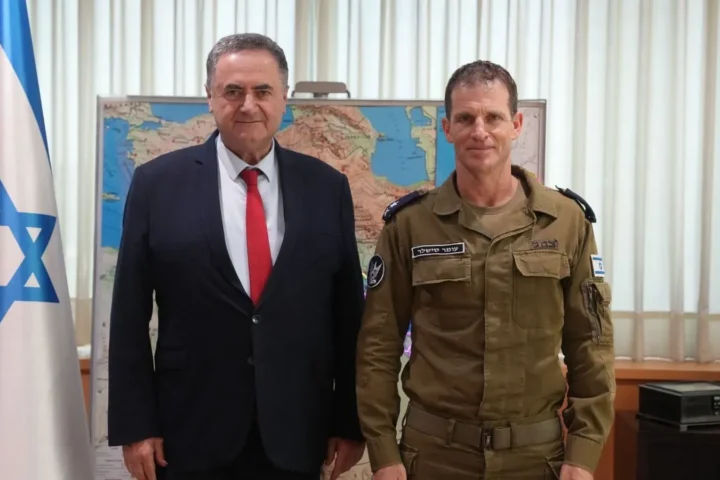 Israeli Defence Minister Israel Katz in a dark suit standing next to an Israeli Air Force officer in front of an Israeli flag and a wall map
