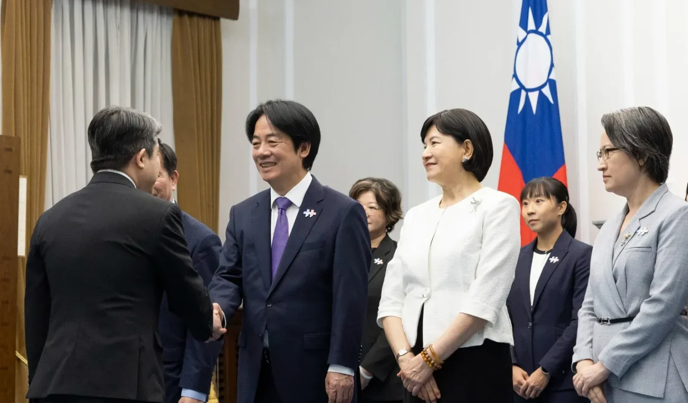 Taiwan’s President Lai Ching-te shakes hands with a guest in front of the flag of Taiwan, with Vice President Hsiao Bi-khim and other officials standing beside him