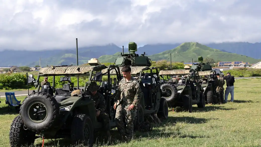 Marines beside L-MADIS vehicles in a field at Marine Corps Base Hawaii with green hills behind