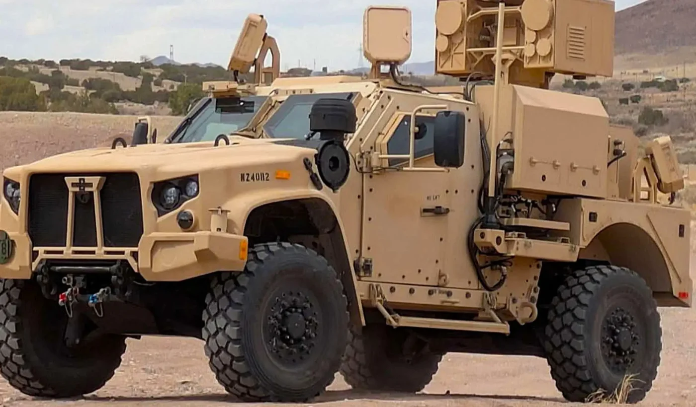 Tan JLTV tactical vehicle fitted with the AeroVironment LOCUST high-energy laser turret and sensors, parked on desert terrain