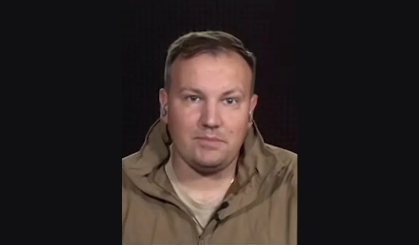 Portrait of Mikhail Zvinchuk, founder of the Russian military blog Rybar, in a tan jacket against a dark background