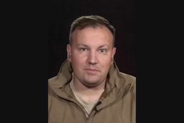 Portrait of Mikhail Zvinchuk, founder of the Russian military blog Rybar, in a tan jacket against a dark background