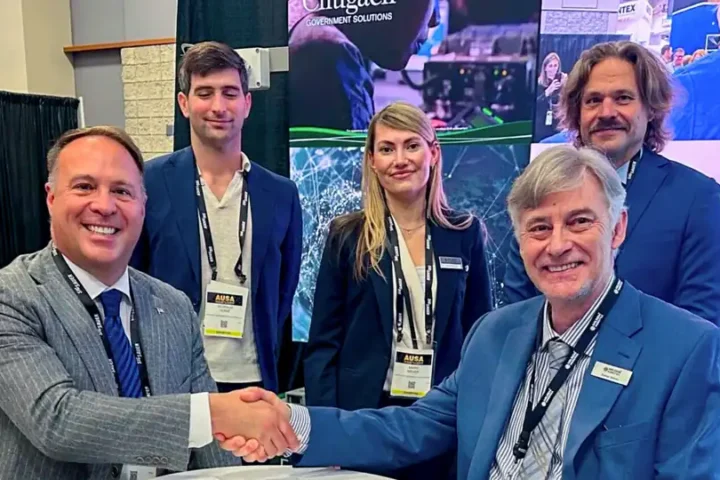 Representatives of Milrem Robotics and Chugach shake hands at a table in front of a Chugach display at the AUSA 2026 exhibition