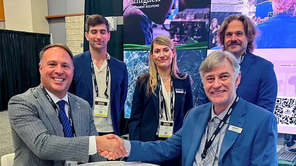 Representatives of Milrem Robotics and Chugach shake hands at a table in front of a Chugach display at the AUSA 2026 exhibition