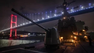The destroyer USS Donald Cook at night on the Bosphorus, with its forward gun in the foreground and an illuminated suspension bridge overhead