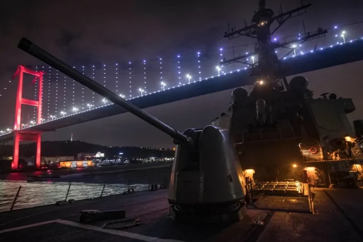 The destroyer USS Donald Cook at night on the Bosphorus, with its forward gun in the foreground and an illuminated suspension bridge overhead
