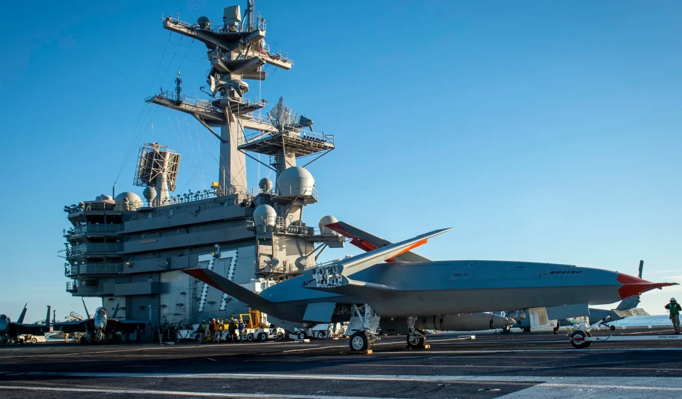 A grey MQ-25 unmanned aircraft on an aircraft carrier flight deck with sailors around it