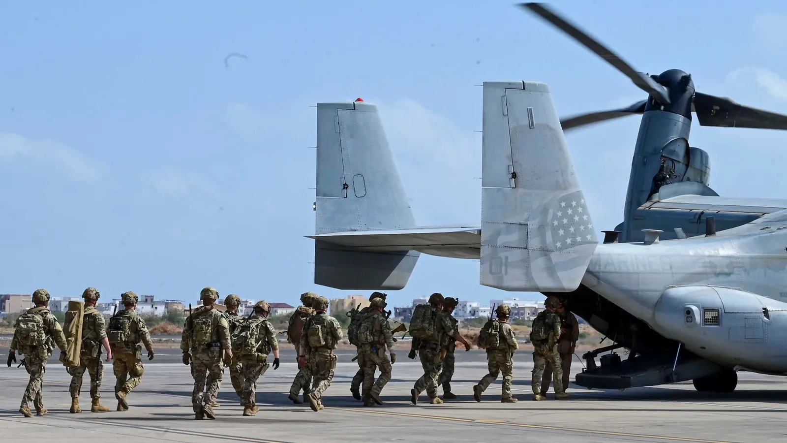 US soldiers in full kit boarding an MV-22 Osprey from its open ramp on an airfield