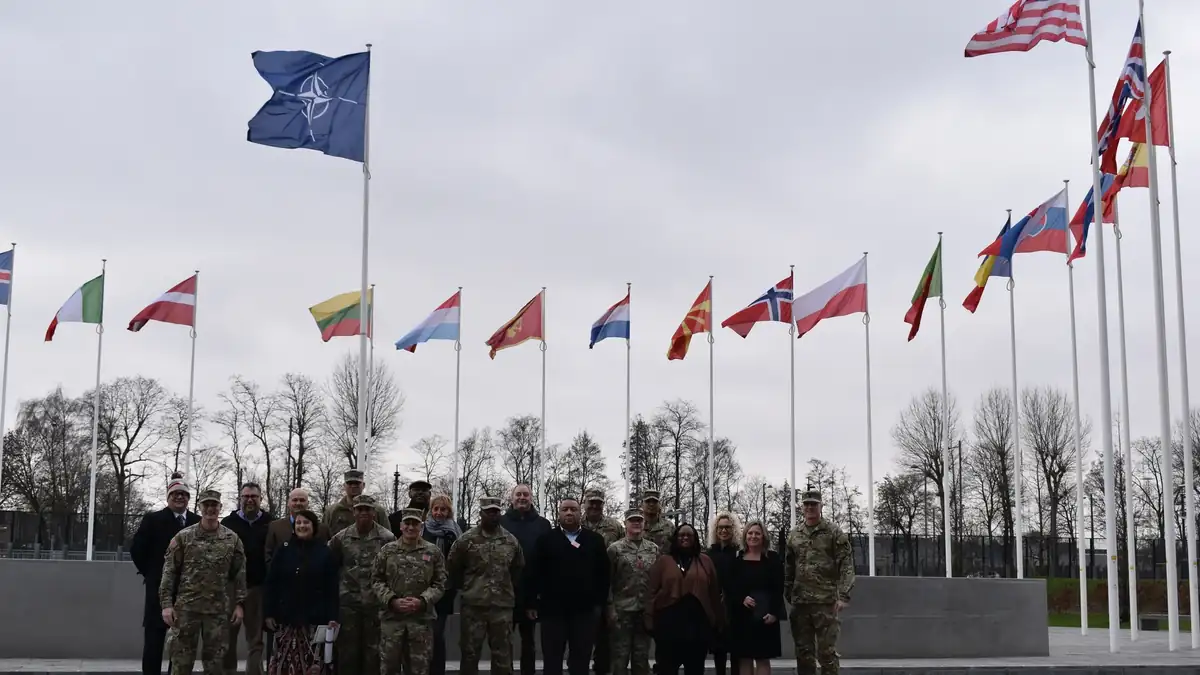 Flags of NATO and its member countries flying outside NATO headquarters in Brussels, with a group of visitors in front