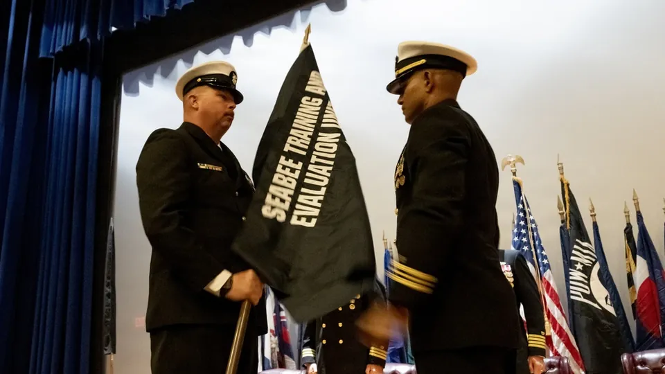 Seabee Training and Evaluation Unit 1 colors being unfurled by two Navy personnel at the commissioning ceremony