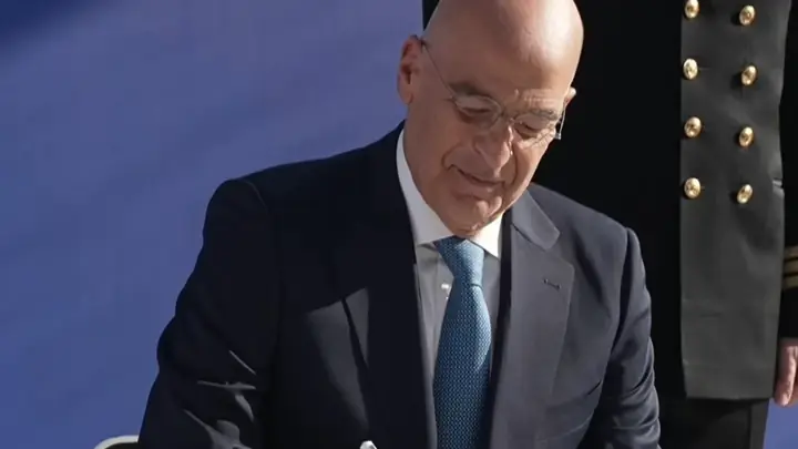 The Greek defence minister Nikos Dendias signs the handover documents for the frigate Nearchos at Lorient, with a Hellenic Navy officer behind him