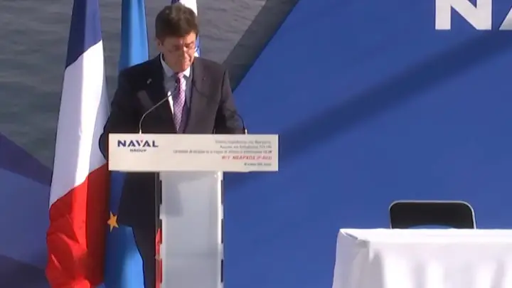 The chairman and CEO of Naval Group Pierre-Éric Pommellet speaks at a lectern with the French and European flags at the Nearchos handover ceremony in Lorient