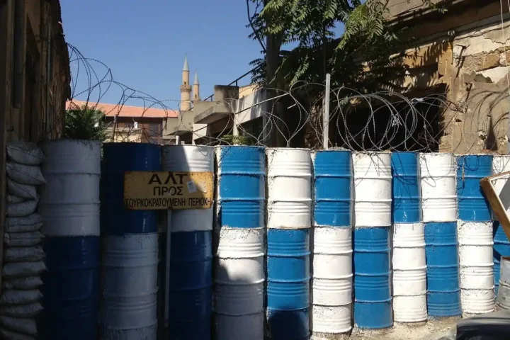 Blue and white painted barrels and coils of barbed wire blocking a street in the UN buffer zone in Nicosia, with a sign reading halt, toward Turkish-occupied area