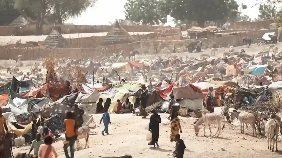 Tents and makeshift shelters at a refugee camp in Chad, with people and donkeys in the foreground
