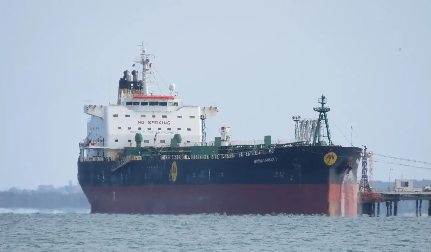 An oil products tanker with a black and red hull and white superstructure moored alongside a refinery jetty