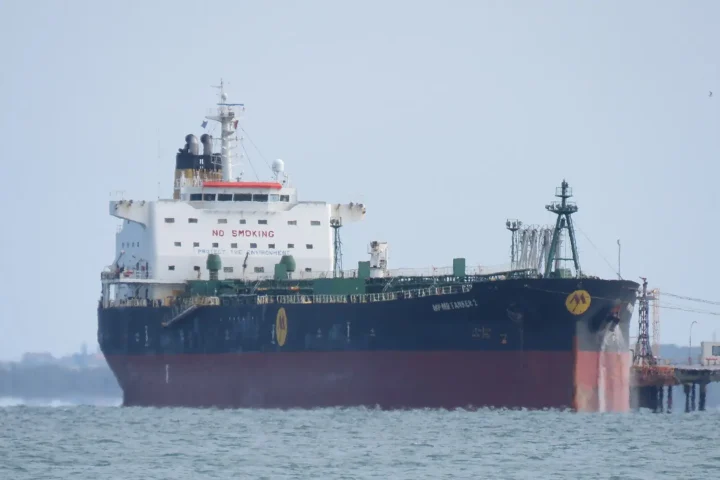 An oil products tanker with a black and red hull and white superstructure moored alongside a refinery jetty