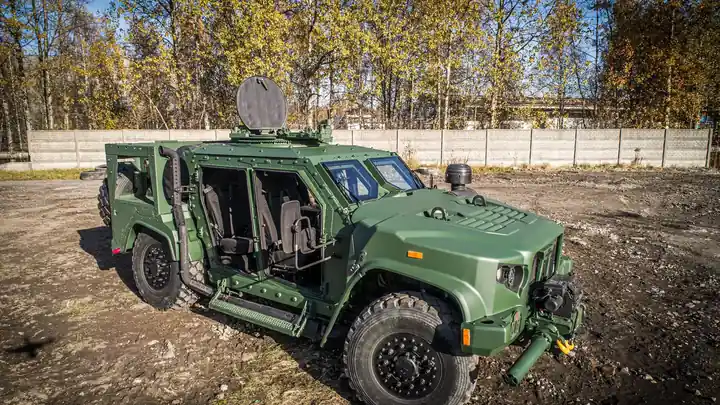 Green Oshkosh Dutch Expeditionary Patrol Vehicle, a JLTV derivative, parked on open ground with autumn trees behind