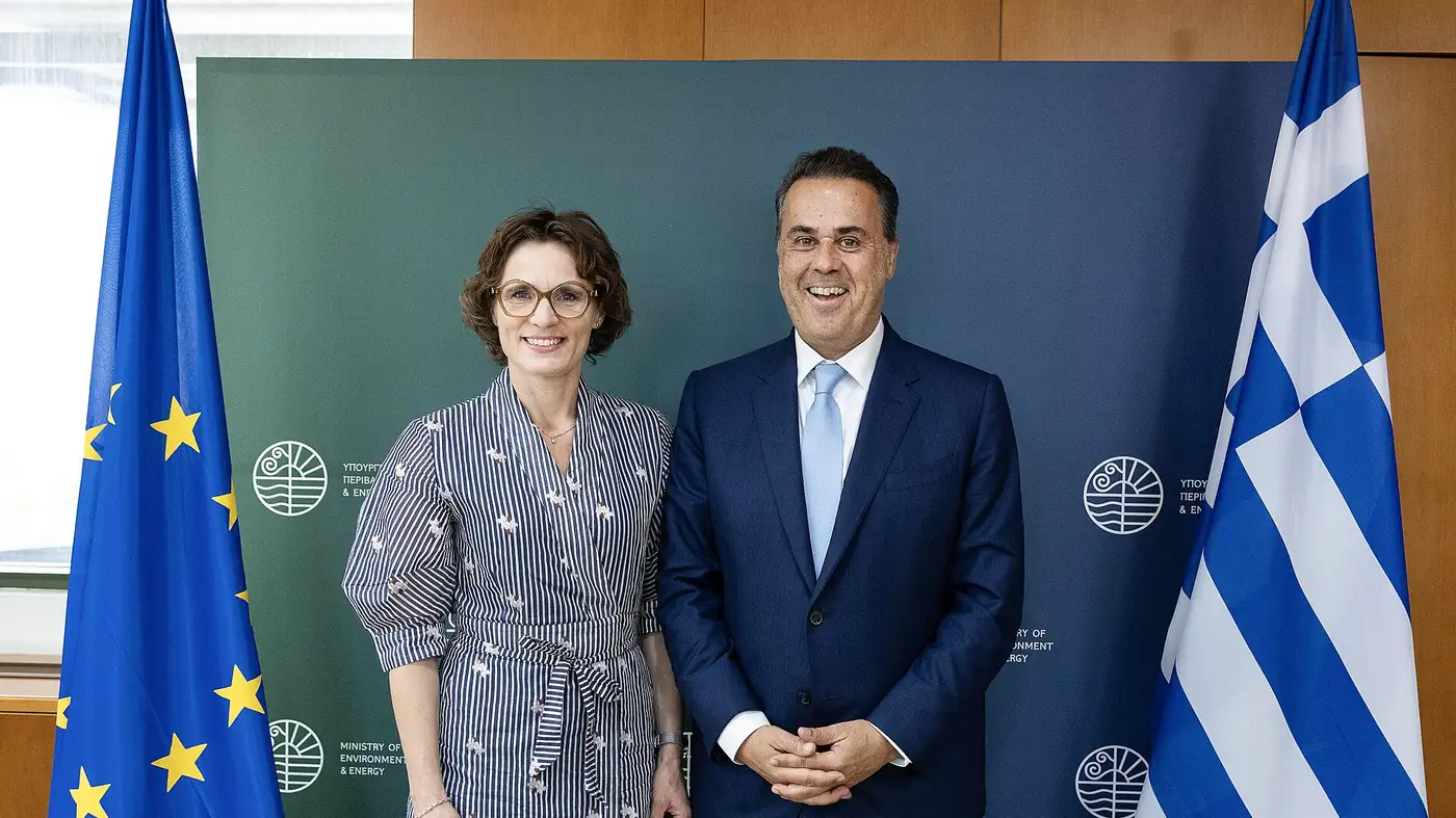 Greek Minister of Environment and Energy Stavros Papastavrou stands beside EU Commissioner Jessika Roswall in front of a ministry backdrop with EU and Greek flags