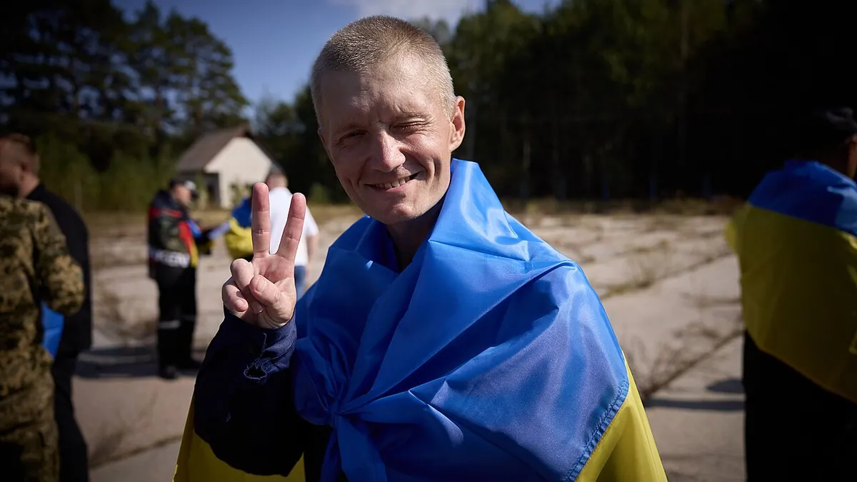 A released Ukrainian prisoner wrapped in the national flag makes a victory sign during an earlier exchange in September 2024