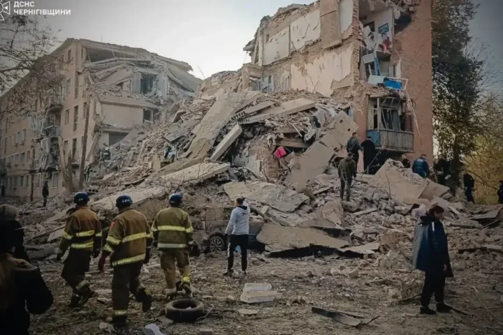 Rescuers and residents stand before the collapsed floors of a five-storey apartment block in Pryluky after a Russian missile strike