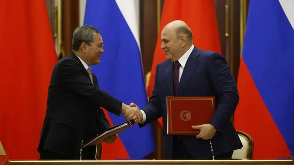 Chinese Premier Li Qiang and Russian Prime Minister Mikhail Mishustin shake hands in front of Chinese and Russian flags at a signing ceremony