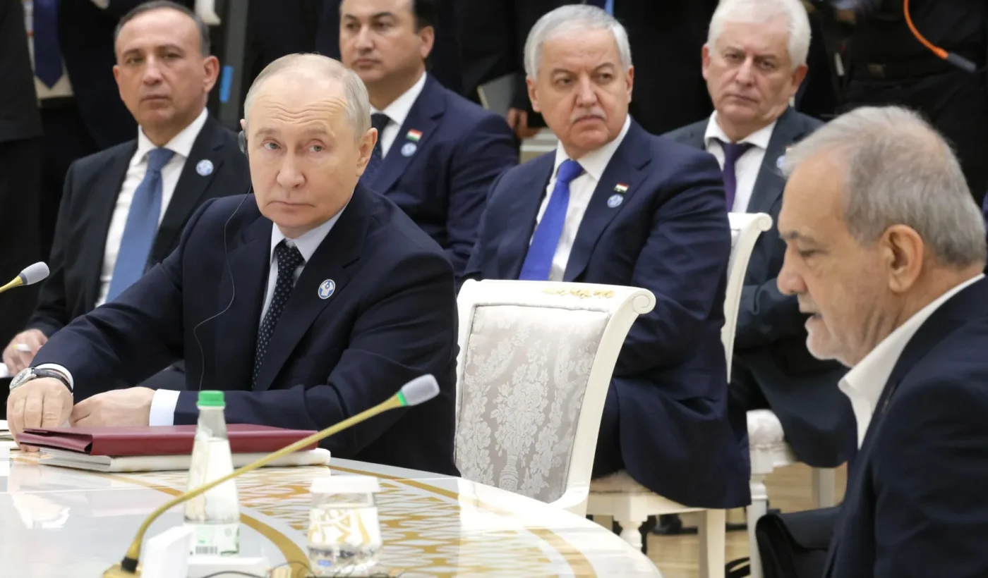 Vladimir Putin seated at a conference table with delegations behind him and Iranian President Masoud Pezeshkian in the right foreground at the CIS summit in Turkmenistan
