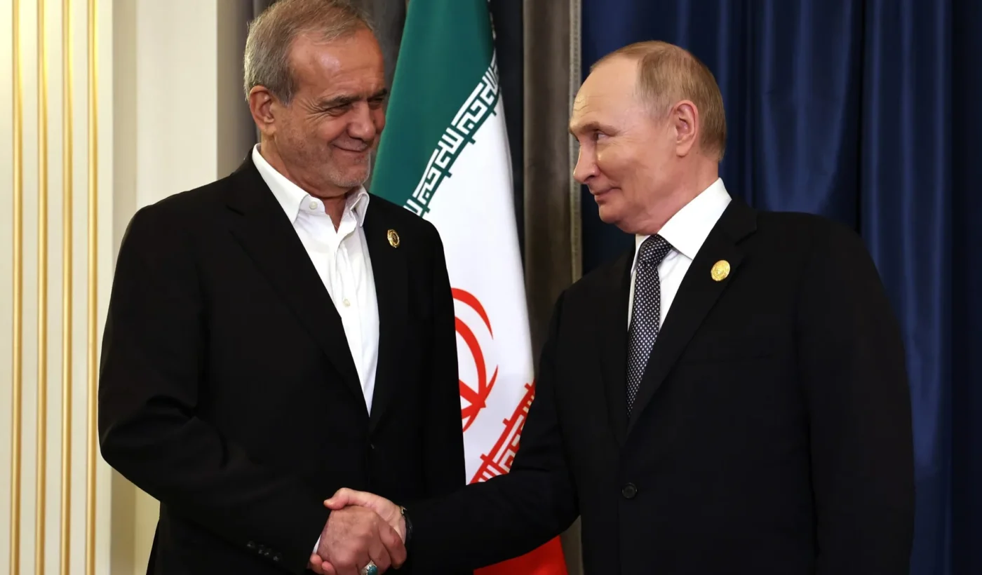 Vladimir Putin and Masoud Pezeshkian shaking hands in front of the flag of Iran
