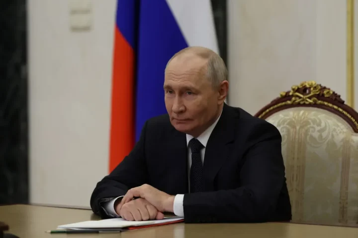 Vladimir Putin sits at a table in the Kremlin in front of a Russian flag during a Security Council videoconference