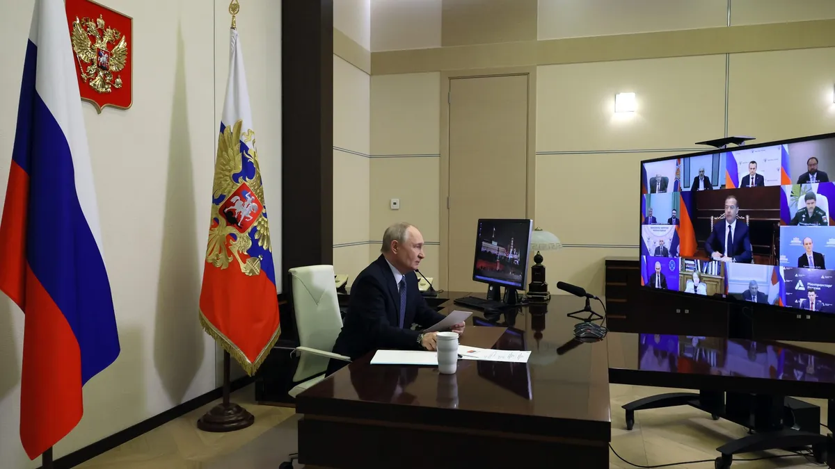 Vladimir Putin seated at a desk in front of Russian flags, taking part in a video meeting at Novo-Ogaryovo