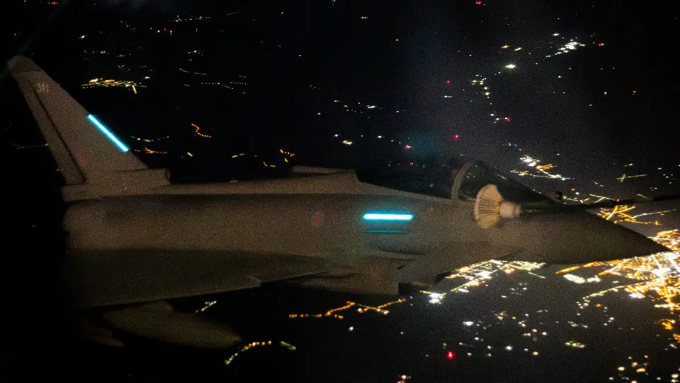 An RAF Typhoon fighter seen at night in flight over lit-up ground, in a file photo from a NATO air mission
