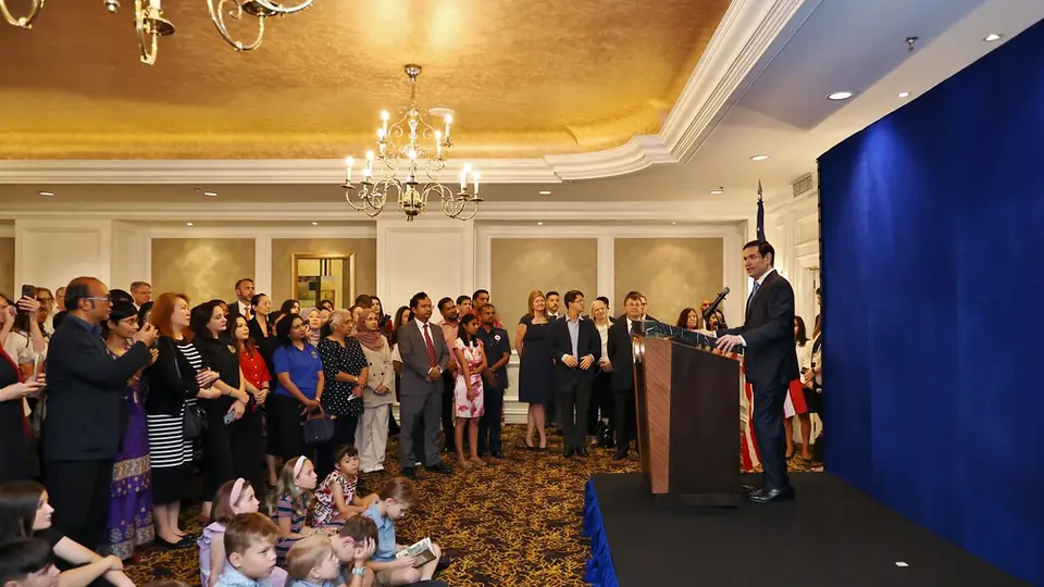 Secretary of State Marco Rubio speaks at a podium before a crowd of embassy staff and families