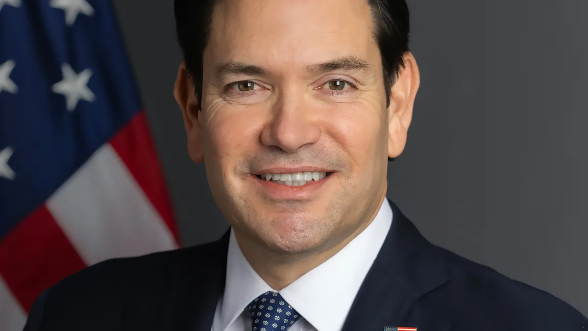 Official portrait of U.S. Secretary of State Marco Rubio in front of a U.S. flag