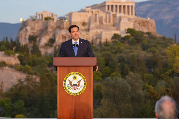 Marco Rubio at a wooden lectern bearing the Department of State seal, with the rock of the Acropolis and its monuments behind him