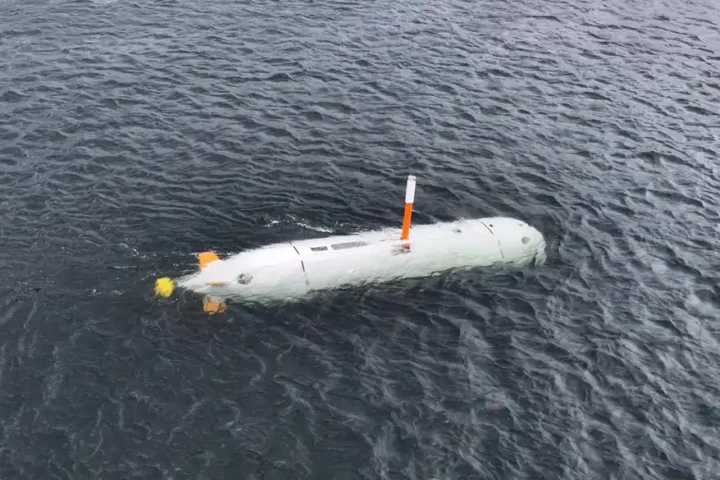 The white hull of an uncrewed underwater vehicle with an orange mast floating on the surface of dark water