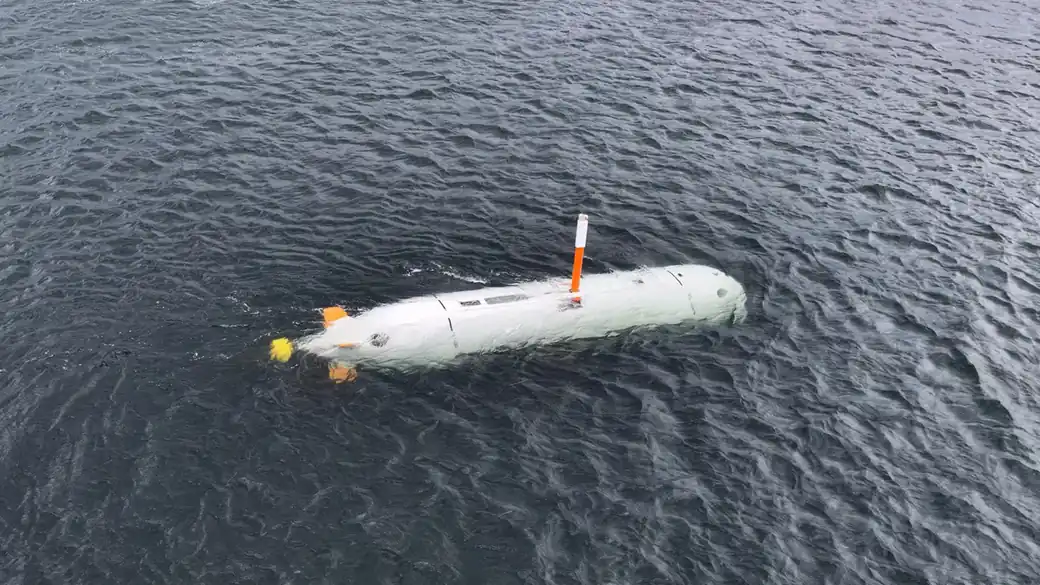 The white hull of an uncrewed underwater vehicle with an orange mast floating on the surface of dark water