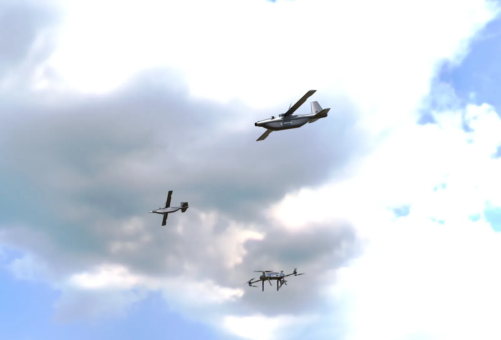 Computer-generated image of a loitering munition and two other unmanned aircraft flying among clouds