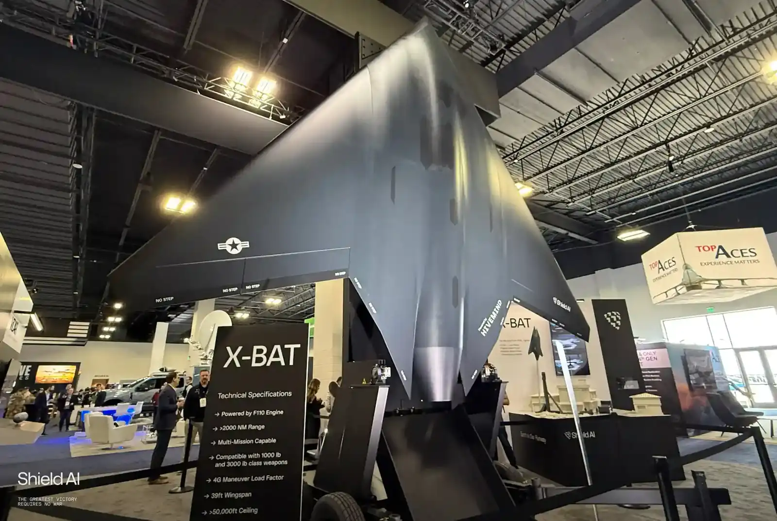 A large dark delta-winged X-BAT model on display at a defence exhibition, beside a sign listing the aircraft’s technical specifications