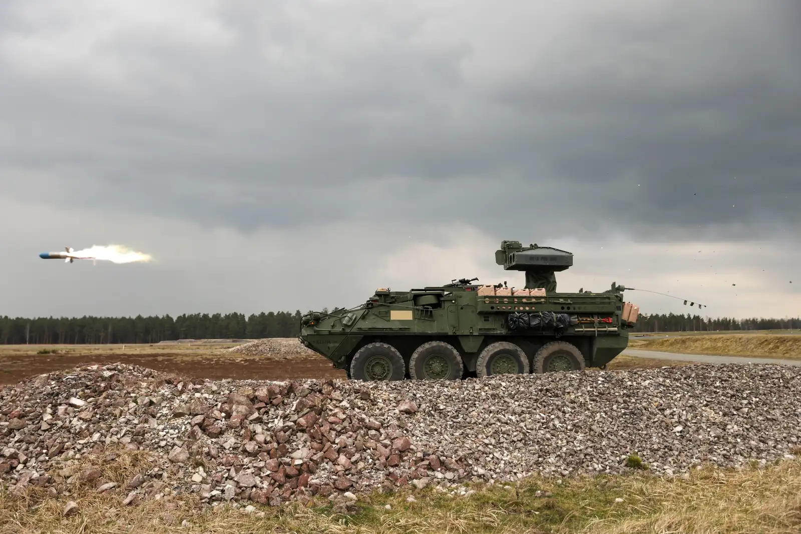 A Stryker anti-tank guided missile vehicle firing a missile on a range, with the missile and its exhaust flame visible to the left