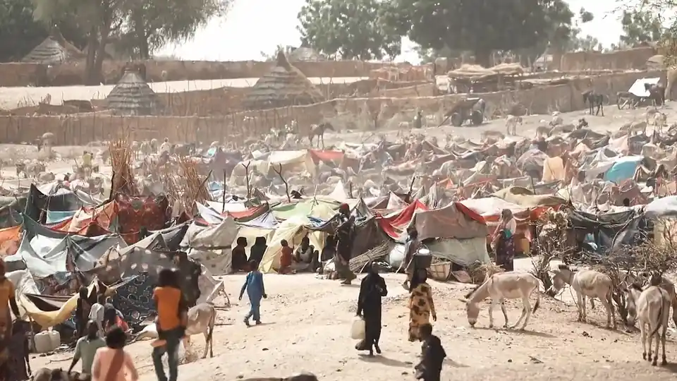 Tents and makeshift shelters at a refugee camp in Chad, with people and donkeys in the foreground