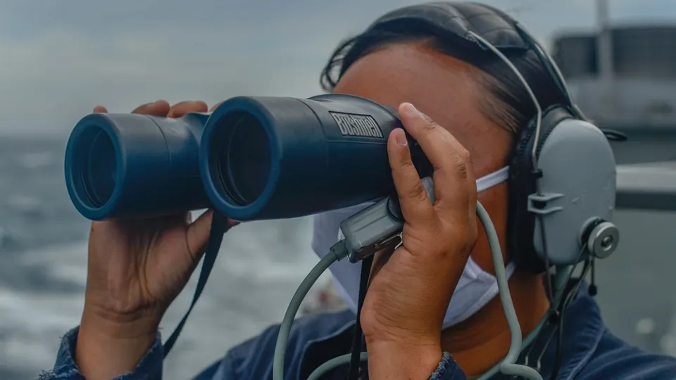 A U.S. Navy sailor looks through binoculars on the bridge wing of the destroyer USS Russell during a Taiwan Strait transit