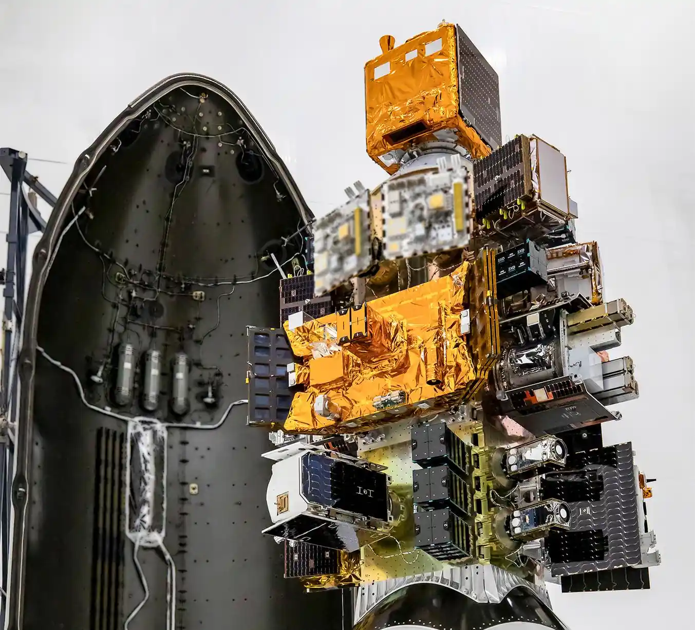 Stack of small satellites mounted on a dispenser beside the open half of a Falcon 9 payload fairing at Vandenberg Space Force Base