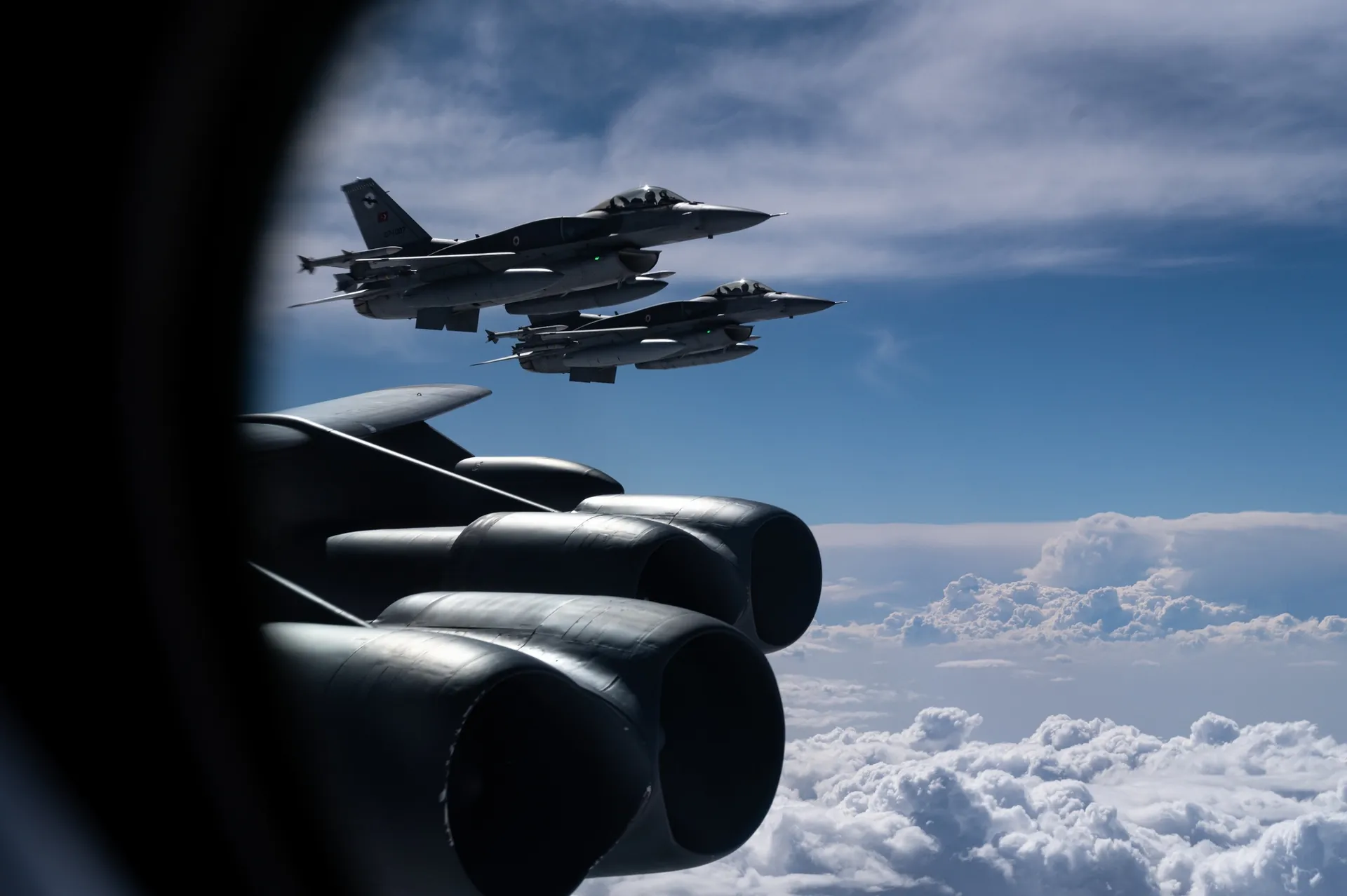 Two Turkish F-16s carrying air-to-air missiles flying in formation beside a US B-52 bomber